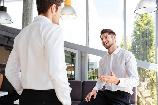 Два улыбающихся бизнесмена стоят и разговаривают в офисе — стоковое фото