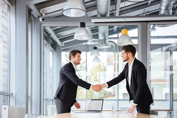 Dos hombres de negocios felices de pie y estrechando la mano en la reunión de negocios —  Fotos de Stock