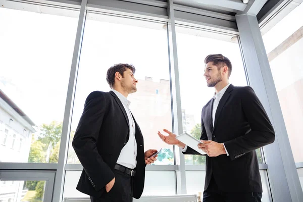 Dos hombres de negocios con tablet y teléfono móvil hablando en la oficina — Foto de Stock