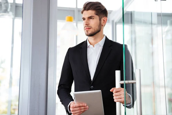 Businesman držení tabletu a vstupu do dveří v úřadu — Stock fotografie