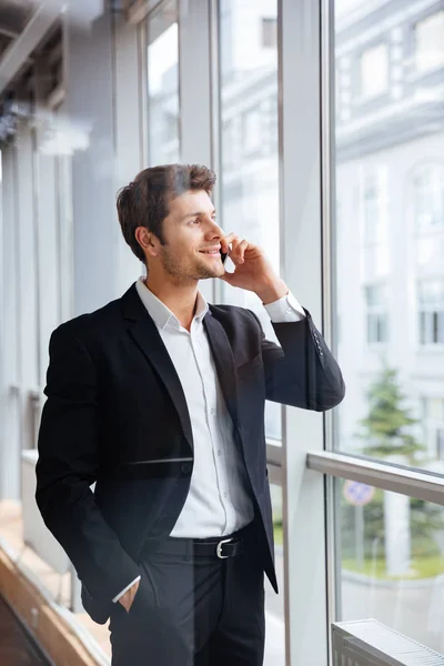 Happy young businessman talking on mobile phone in office — Stock Photo, Image