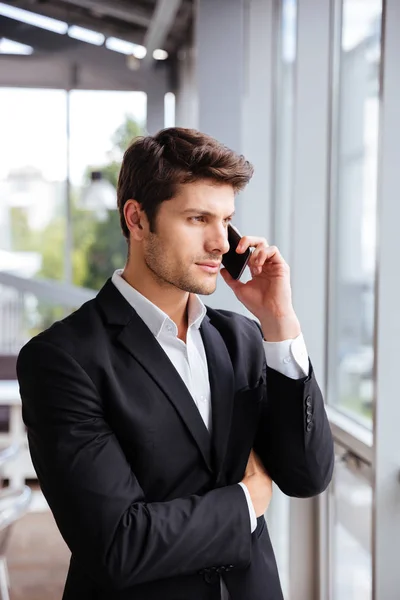 Ernstige jonge zakenman praten op mobiele telefoon in kantoor — Stockfoto