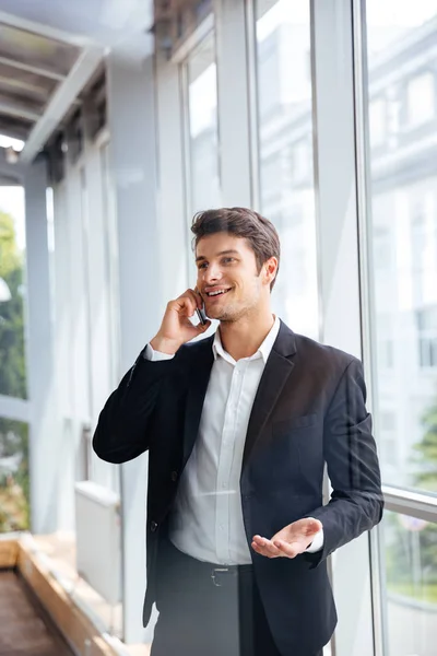 Jovem empresário alegre falando no celular no escritório — Fotografia de Stock