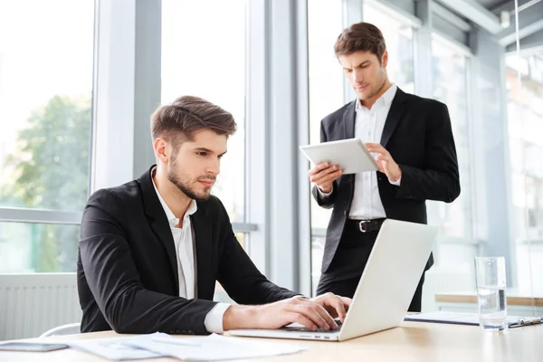 Dos hombres de negocios que trabajan con el ordenador portátil y tableta en la oficina —  Fotos de Stock