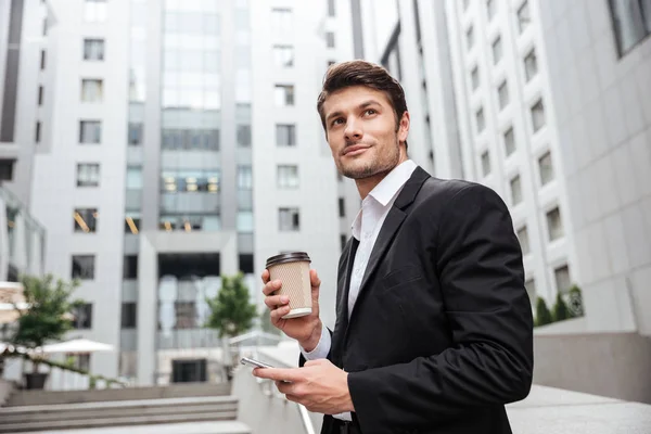 Empresario con tomar café de pie y el uso de teléfono móvil —  Fotos de Stock