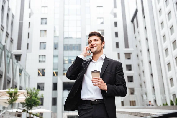 Joven empresario alegre hablando por teléfono celular y tomando café — Foto de Stock
