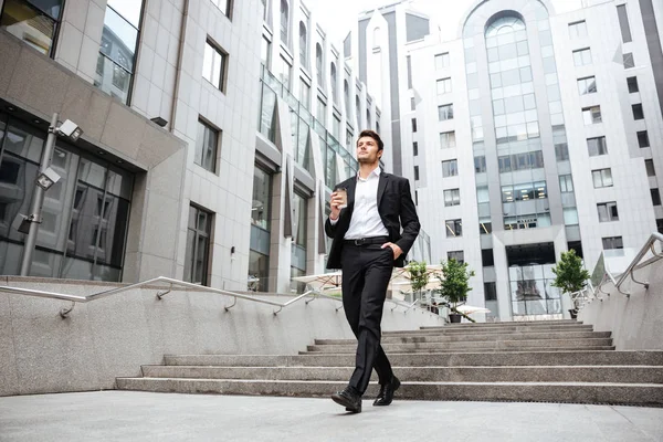 Empresario caminando y tomando café cerca del centro de negocios —  Fotos de Stock