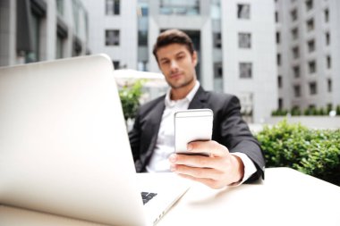 Dizüstü bilgisayar ve cep telefonu açık kafede kullanarak iş adamı