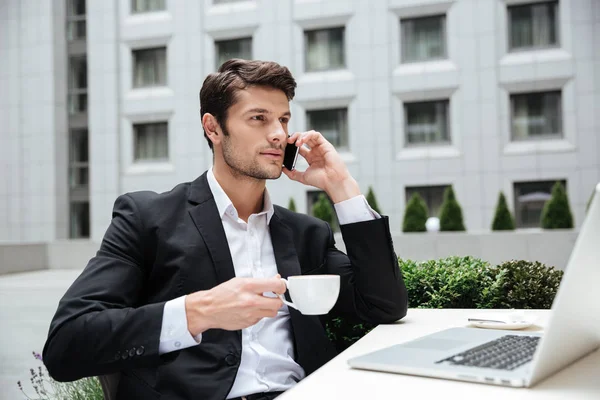 Бизнесмен разговаривает по мобильному телефону и пьет кофе в кафе — стоковое фото