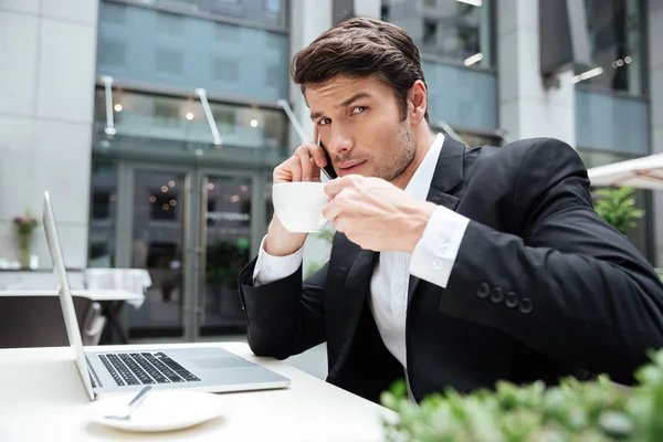 Uomo d'affari con laptop che parla al cellulare e beve caffè — Foto Stock