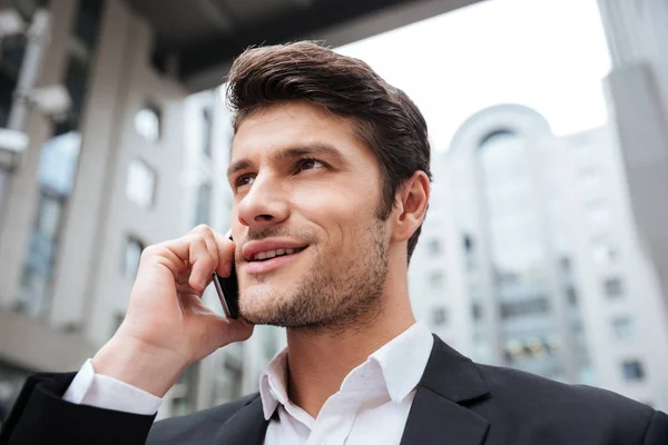 Cheerful attractive young businessman talking on cell phone outdoors — Stock Photo, Image