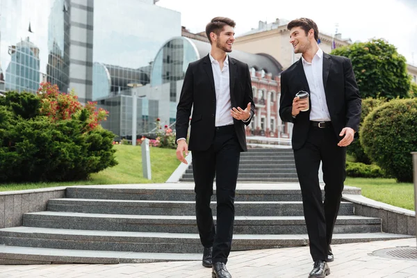 Two businessmen with take away coffee walking and talking outdoors — Stock Photo, Image