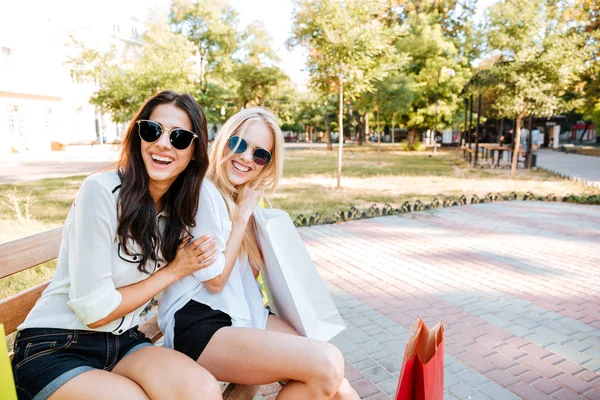 Två vackra flickor i solglasögon vilar på bänk efter shopping — Stockfoto