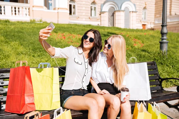 Dos amigos tomando selfie mientras descansan en el banco después de ir de compras —  Fotos de Stock