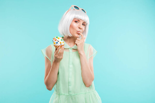Happy playful woman in blonde wig tasting cupcake by finger