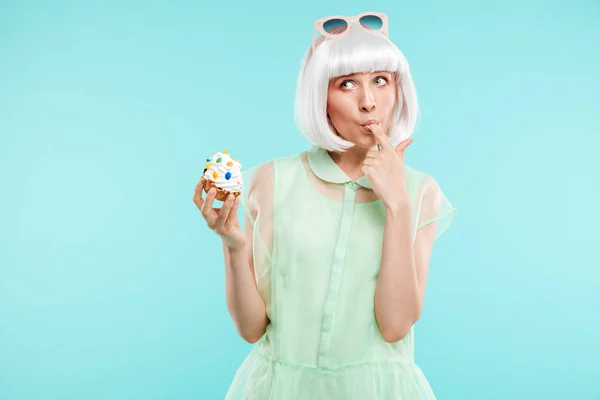 Rolig blond ung kvinna stående och provsmakning cupcake av finger — Stockfoto