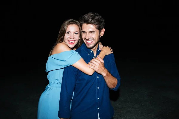 Fröhliches junges Paar, das sich nachts am Strand umarmt — Stockfoto