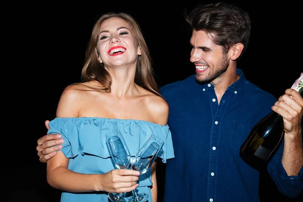 Радостная пара, держа бокалы и бутылку шампанского ночью — стоковое фото