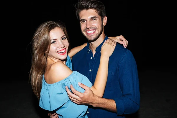 Alegre hermosa pareja joven de pie en la playa por la noche — Foto de Stock