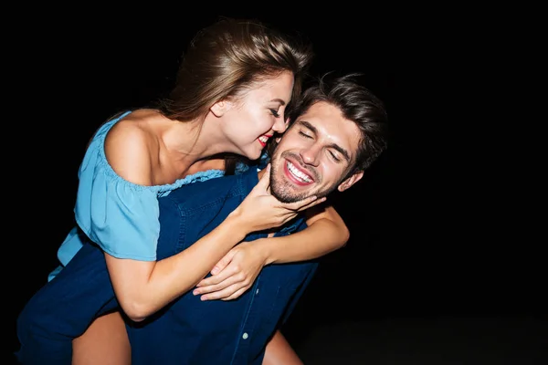 Fröhlicher junger Mann hält Freundin nachts auf dem Rücken — Stockfoto