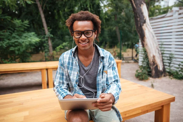 Joven africano alegre usando tableta y sonriendo en el parque — Foto de Stock