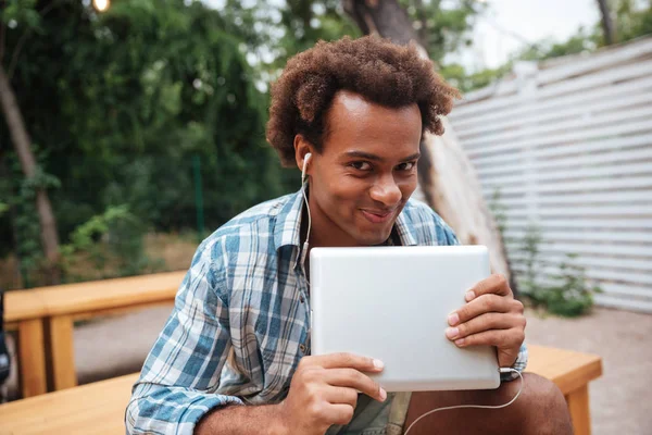 Sonriente joven africano lindo con tableta escuchando música — Foto de Stock