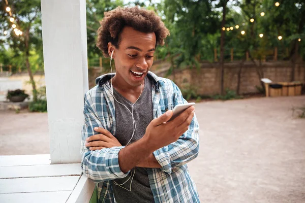 Happy zdziwiony człowiek w słuchawki za pomocą telefonu komórkowego, na zewnątrz — Zdjęcie stockowe