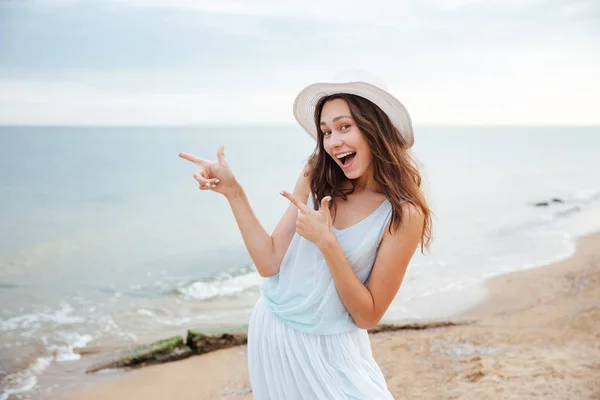 Joyeux jeune femme debout et pointant du doigt sur la plage — Photo