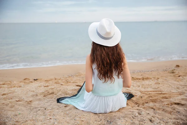 Vista trasera de una joven sentada en la playa — Foto de Stock