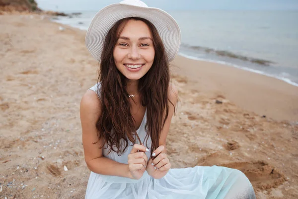 흰 드레스와 모자 해변에 앉아 웃는 여자 — 스톡 사진