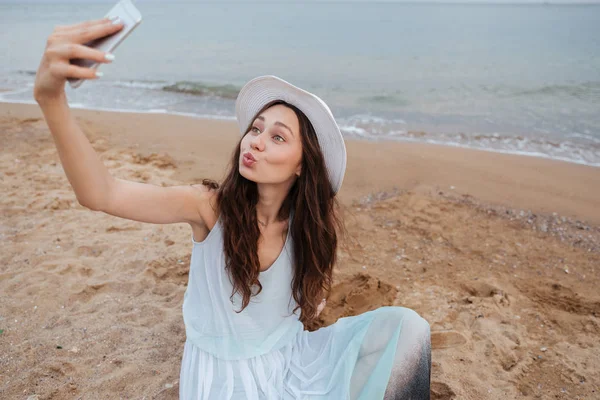 Забавная женщина делает селфи с телефоном на пляже — стоковое фото