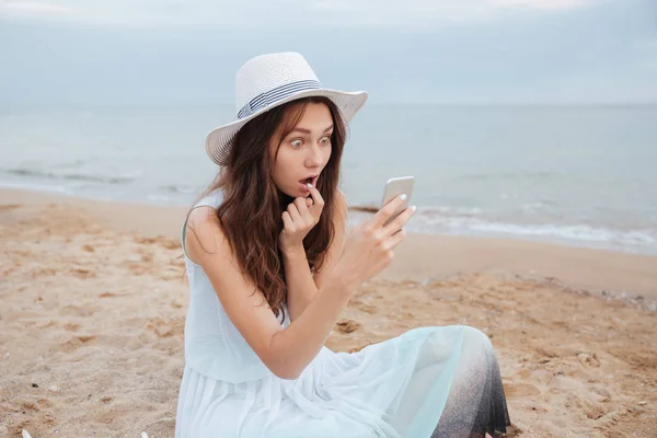 Geschokt vrouw met behulp van mobiele telefoon op het strand — Stockfoto