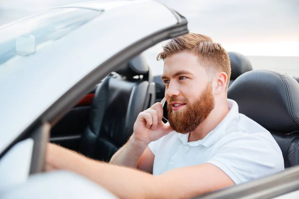 Молодой человек водит свою машину и говорит по мобильному телефону — стоковое фото