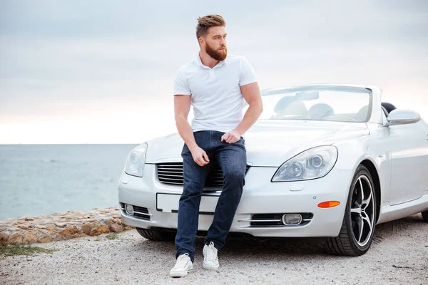 Молодой бородатый мужчина опирается на свою машину — стоковое фото