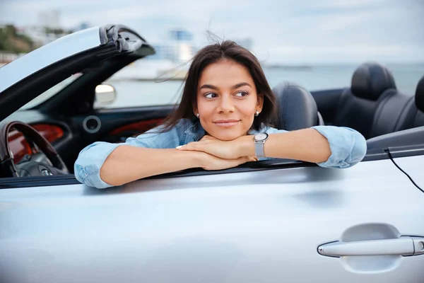 Mujer joven sonriente sentada dentro de su coche descapotable — Foto de Stock