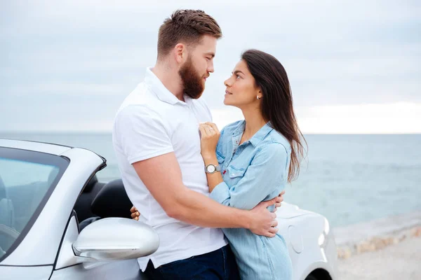 Pareja joven abrazándose mientras está de pie cerca del coche en la playa — Foto de Stock