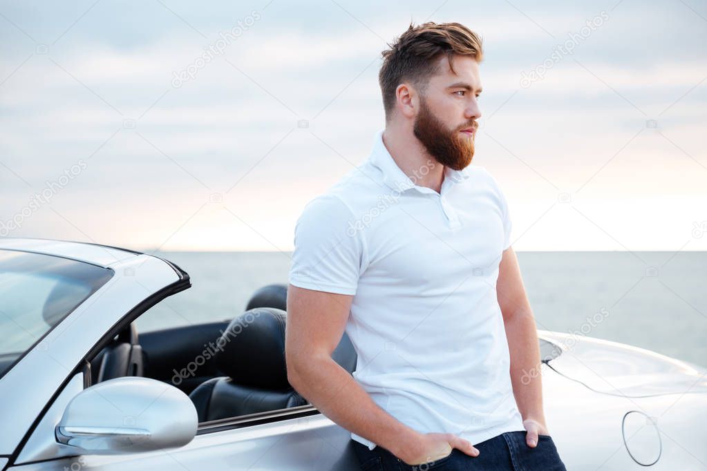 Handsome bearded man in white shirt leaning on car outdoors