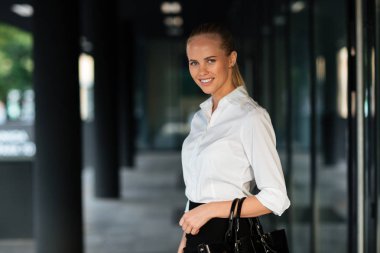 Ayakta ve el çantası koşullarının genç gülümseyen iş kadını