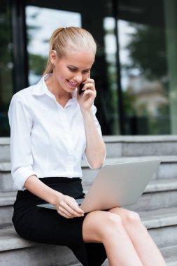 Dizüstü bilgisayar ve telefon merdivenlerde oturan işkadını