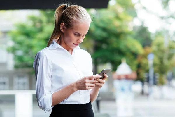 Thoughtful young businesswoman holding mobile phone and typing message — Stock Photo, Image