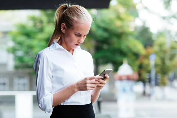 Promyšlené mladá podnikatelka držení mobilního telefonu a psaní zpráv — Stock fotografie