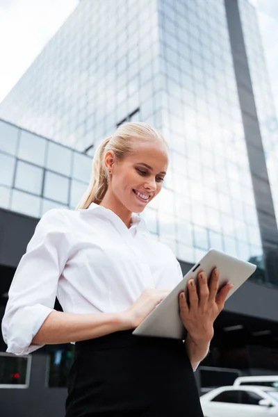 Jonge Glimlachende zakenvrouw met behulp van Tablet PC staande op kantoor — Stockfoto