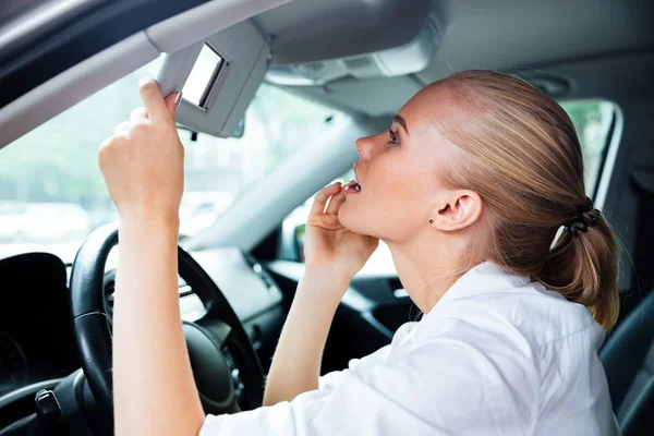 Hübsche junge Geschäftsfrau schaut während der Autofahrt in den Spiegel — Stockfoto
