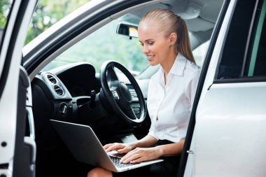 İş kadını arabaya oturma ve çalışma sırasında dizüstü bilgisayar kullanarak