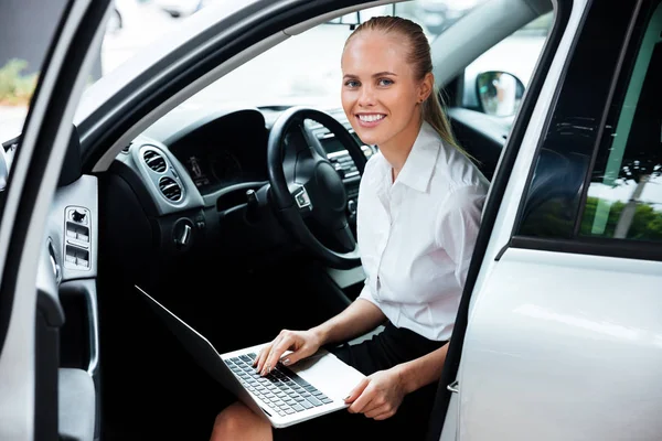 Felice donna d'affari sorridente seduta in auto e che lavora con lapt — Foto Stock