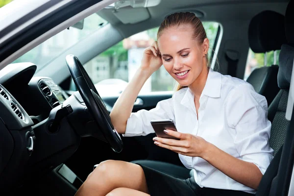 Mujer de negocios sonriente marcando el número de teléfono mientras está sentado en el coche —  Fotos de Stock