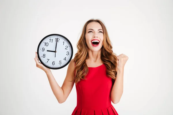 Woman in red dress holding wall clock and celebrating success — Stock Photo, Image