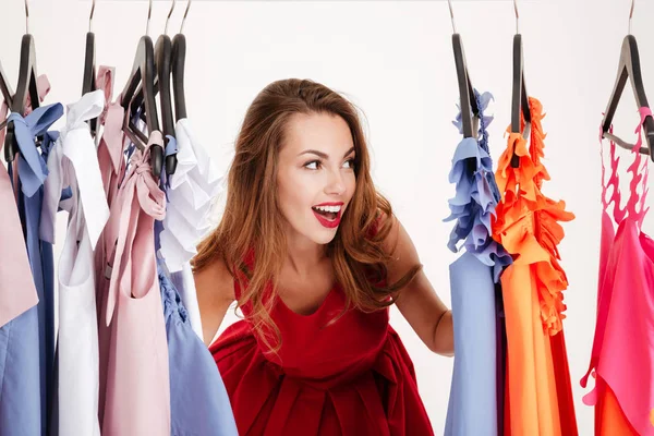 Smiling blonde woman standing inside wardrobe rack full of clothes Stock Image
