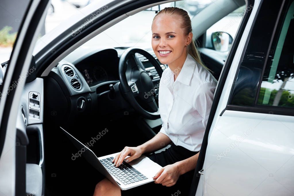 Happy smiling businesswoman sitting in car and working with lapt