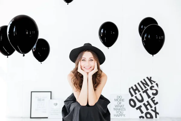 Sorrindo mulher atraente em chapéu com balões de ar preto sentado — Fotografia de Stock